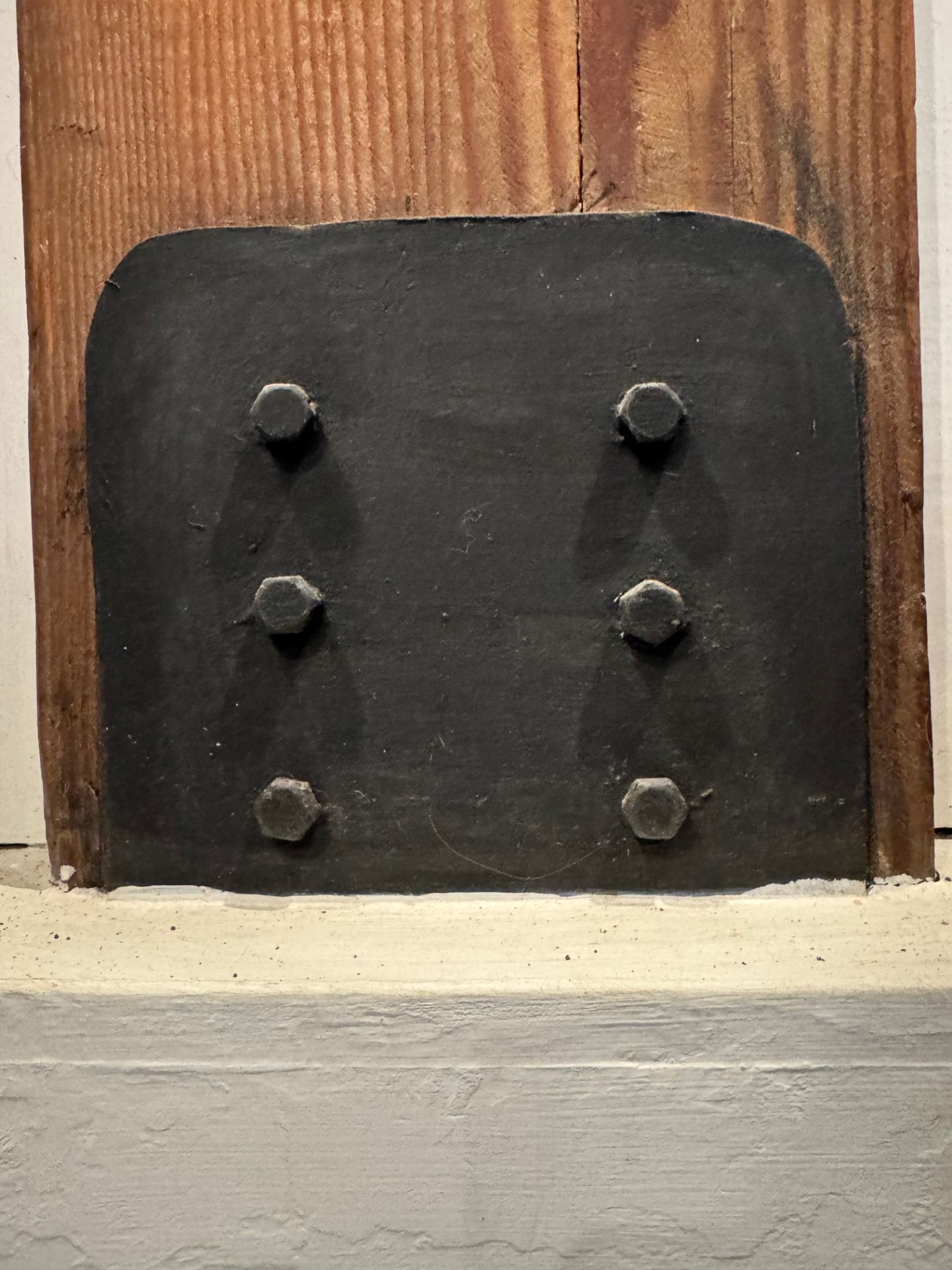 Blackened steel plate bolted to a timber column meeting a lime-washed stone base