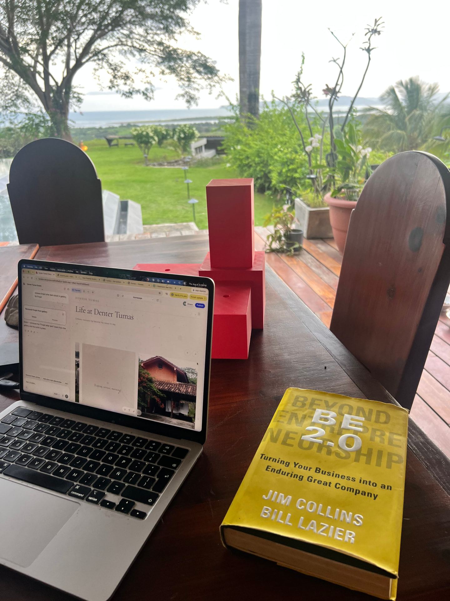 Laptop on the wooden terrace with the garden, pool and hills in the morning light