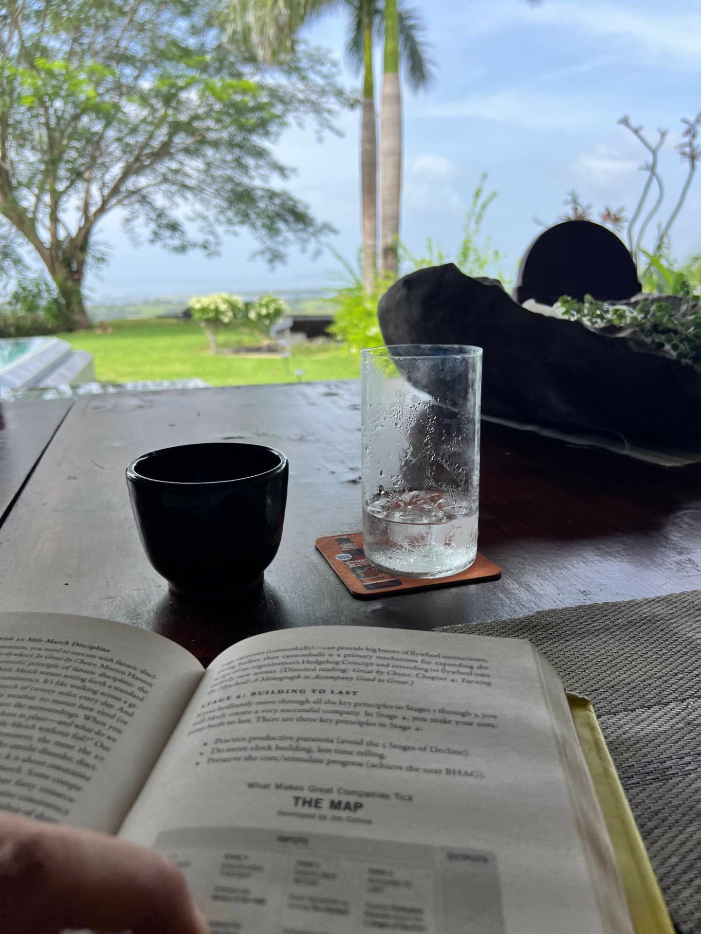 Coffee, water and an open book on the terrace table at Denter Tumas, looking out over the garden to the ocean