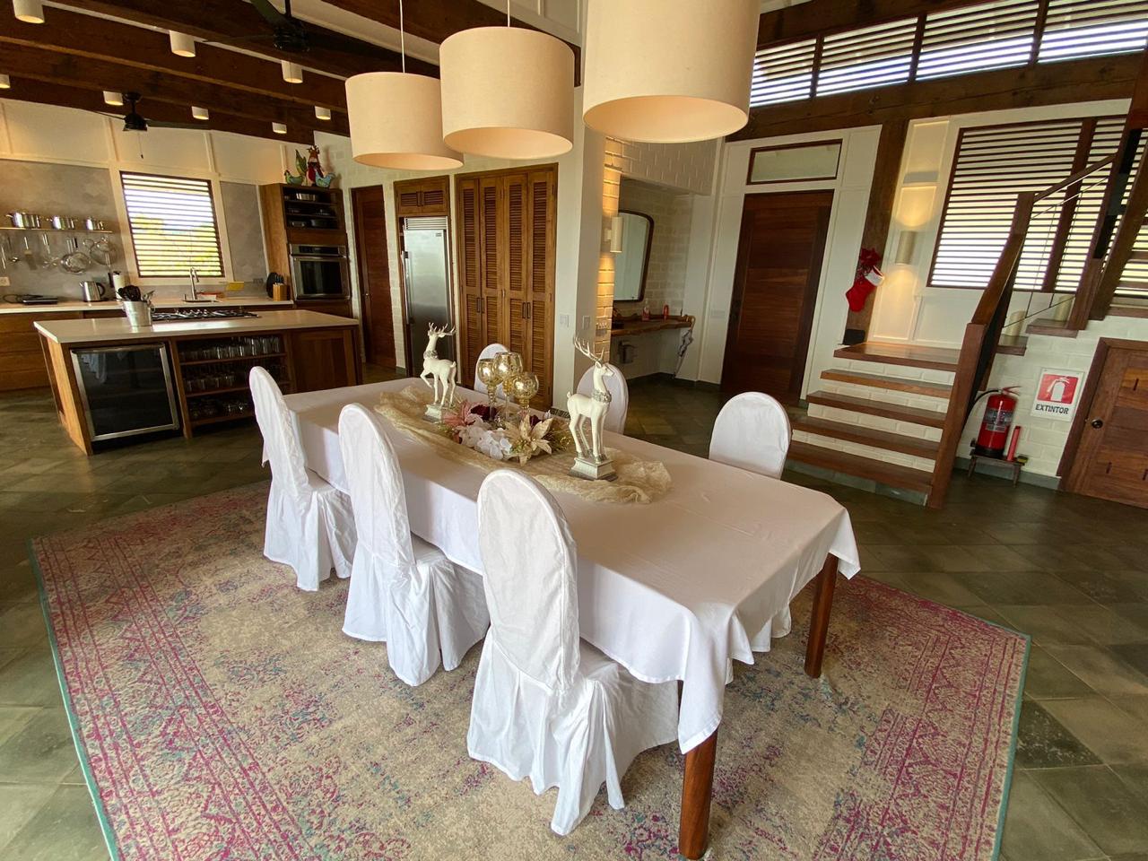 Long dining table set for a meal in the open living room at Denter Tumas, with doors open to the garden
