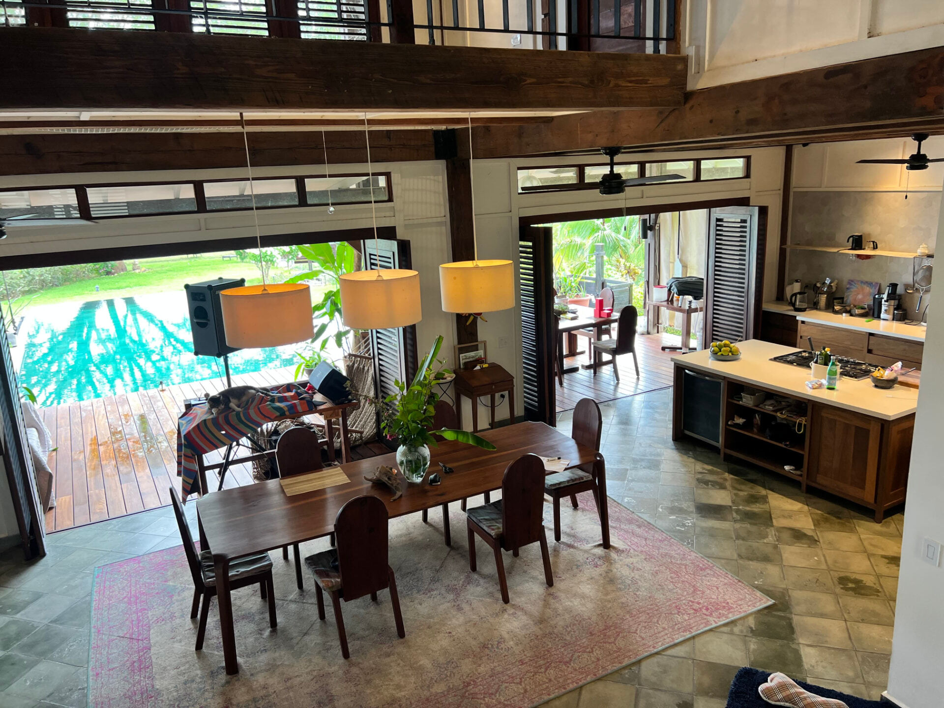 Open-plan kitchen and dining room with timber beams, doors folded open to the pool and garden