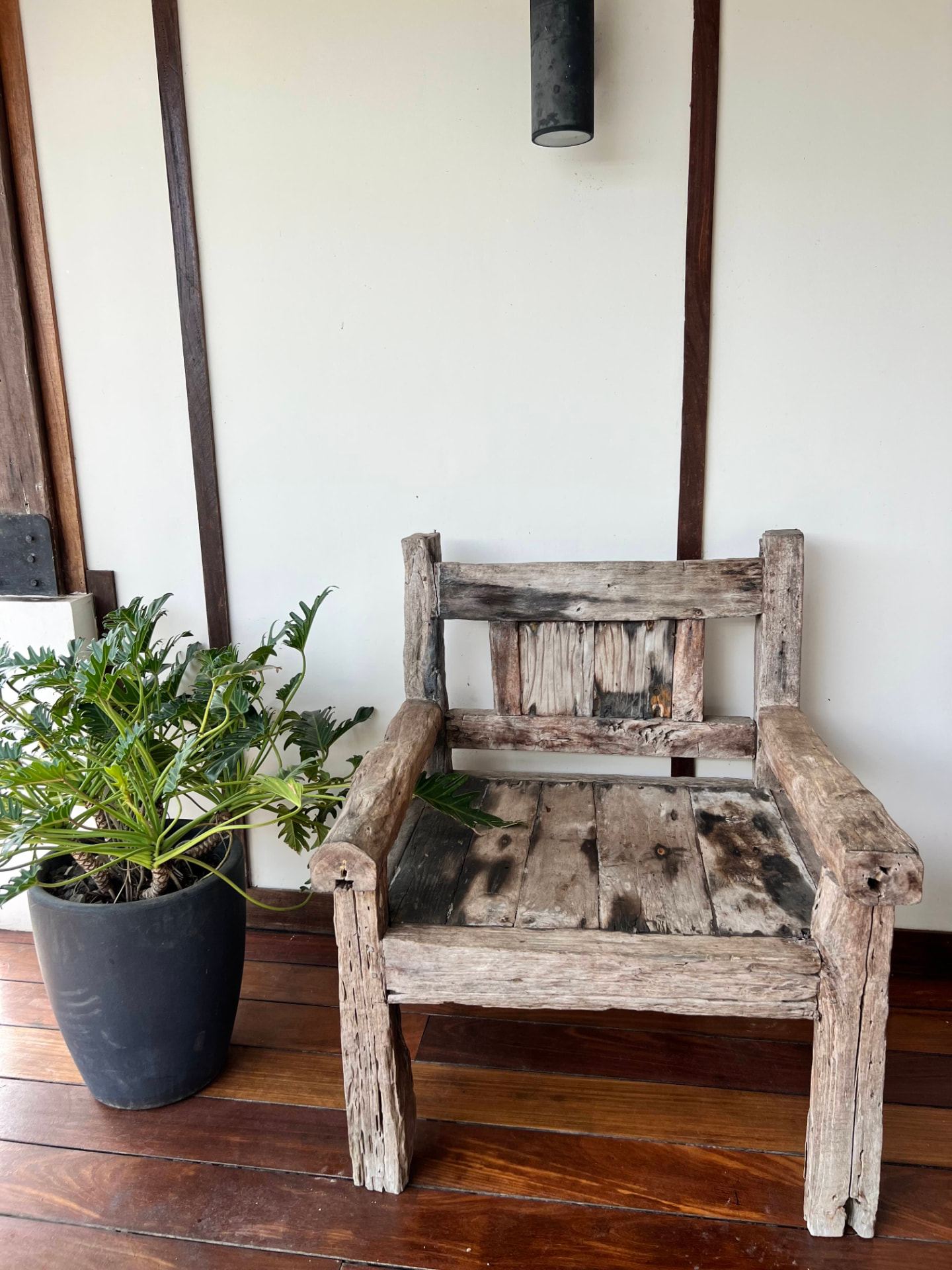 Weathered reclaimed-timber armchair beside a potted plant on the polished hardwood deck at the back of the main house