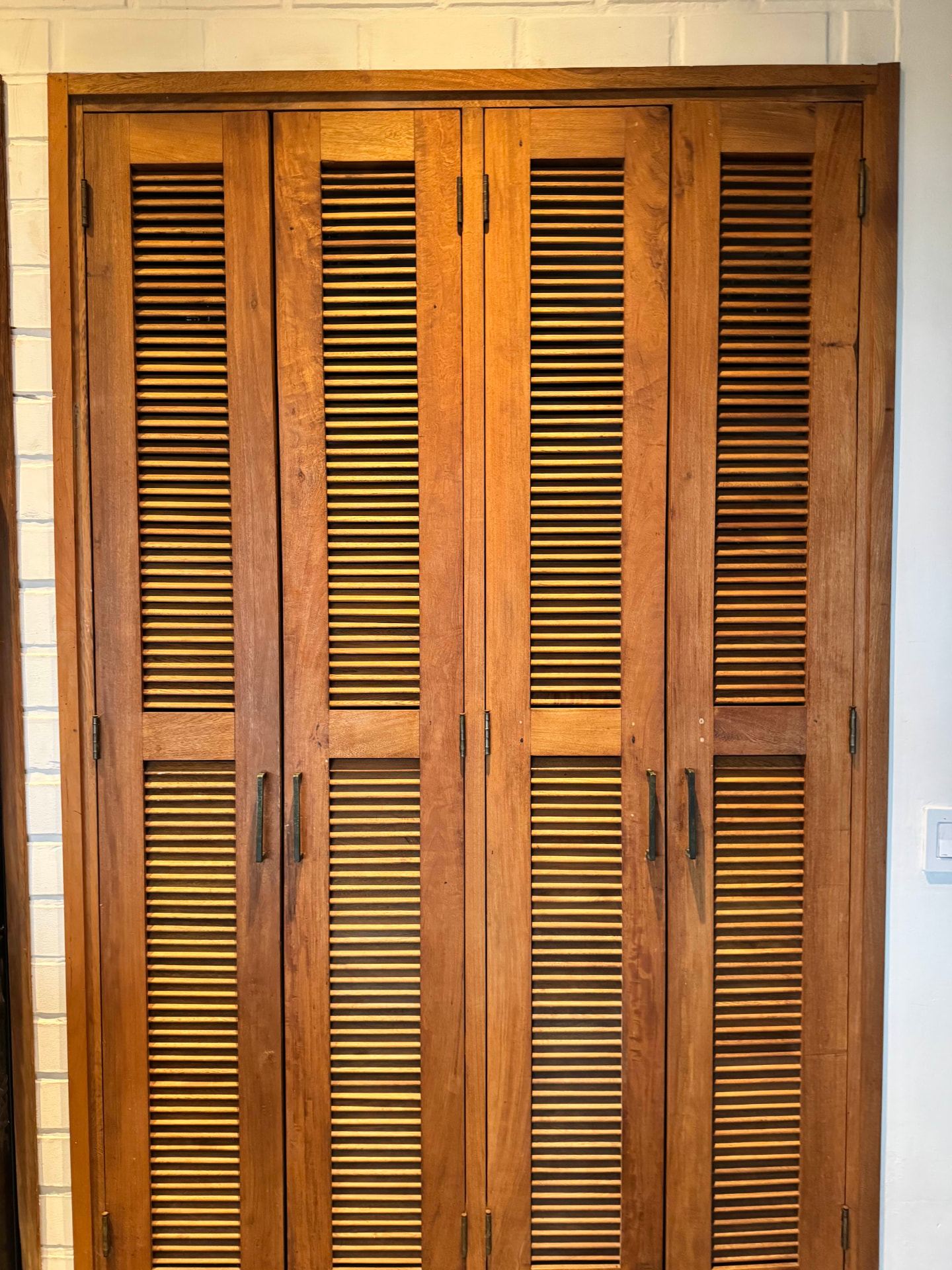 Tall louvred tropical hardwood doors set into a lime-washed stone wall
