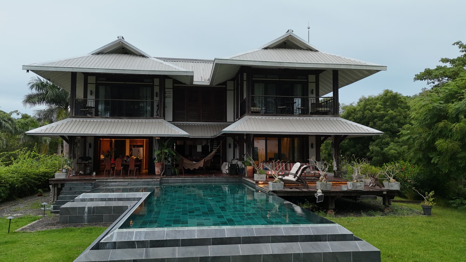 The main villa's twin pavilions at dusk with warm interior light and the green-tiled pool in the foreground