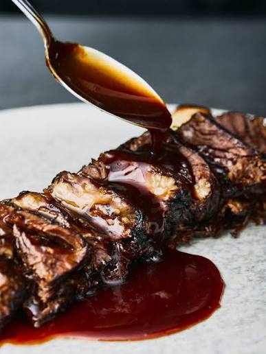 Spoon glazing slow cooked short rib with dark sauce on a stone plate at De Mar restaurant